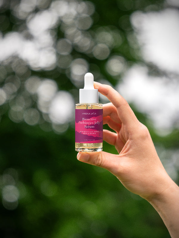 Hand holding a MORA  ATA Bioactive Prebiotics Jelly Serum dropper bottle against a blurred natural background