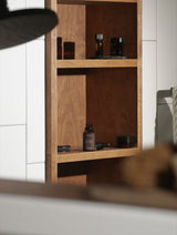 Wooden shelf with skincare products against a white tiled wall featuring a Mora Ata The Styler's Beard Oil bottle with its dropper.